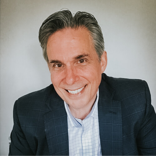 A headshot of a man in a blue suit and button down smiling.